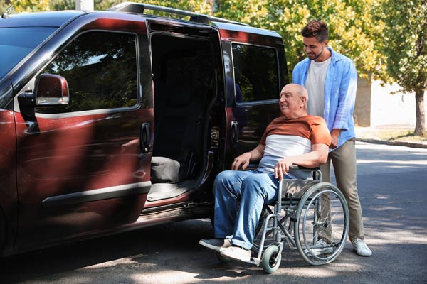 Young man helping patient in wheelchair to get into van outdoors on their way to Special Care Dentistry of Oregon in Albany, OR