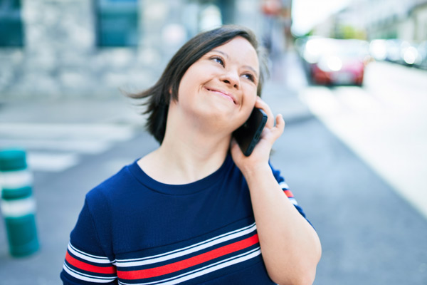 Brunette woman with down syndrome at the town on a sunny day talking on smartphone