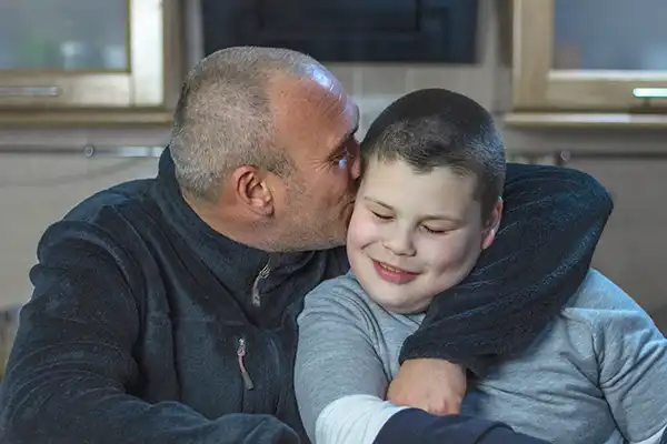 A man with short hair hugs his son and kisses him on the cheek