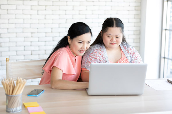 Teenage girl with down syndrome and her teacher using laptop computer together on a table